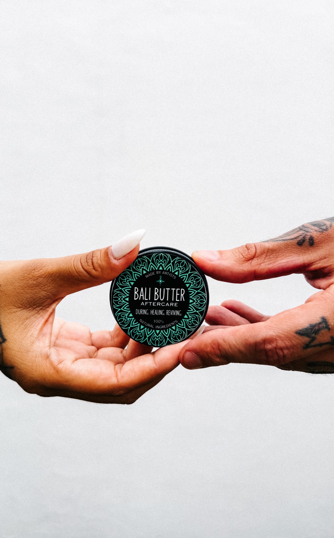 Bali Butter tattoo aftercare tin held between tattooed hands